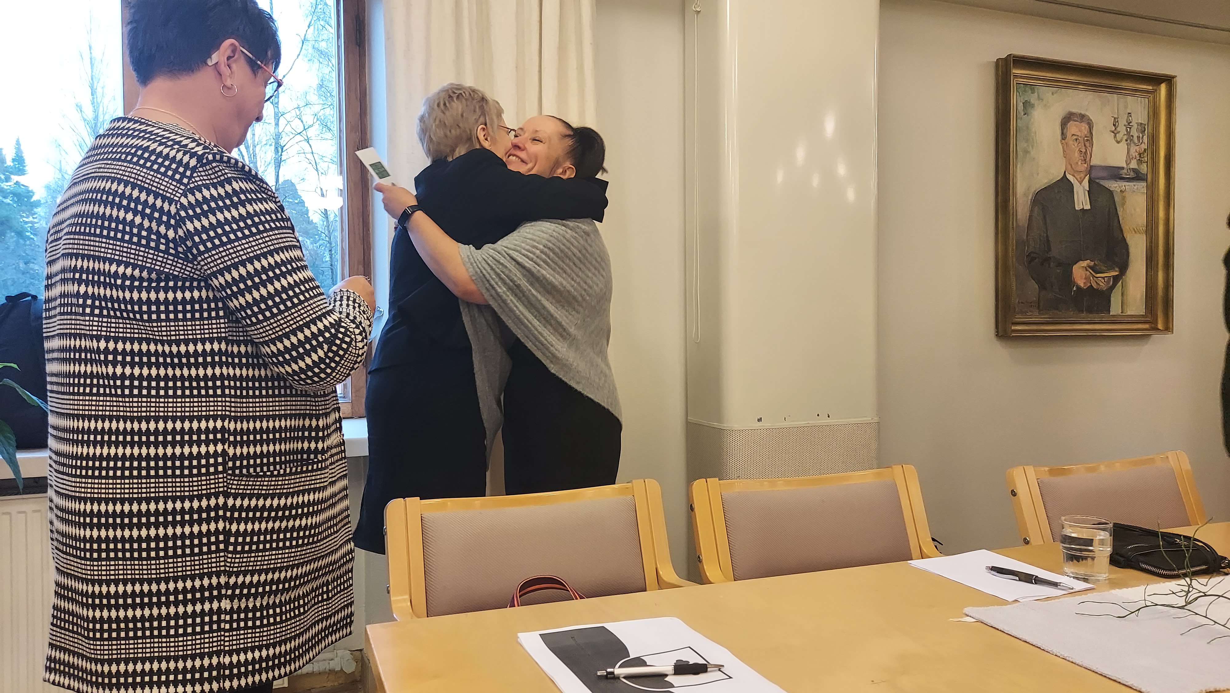 Nainen etualalla ja taka-alalla kaksi naista halaamassa.