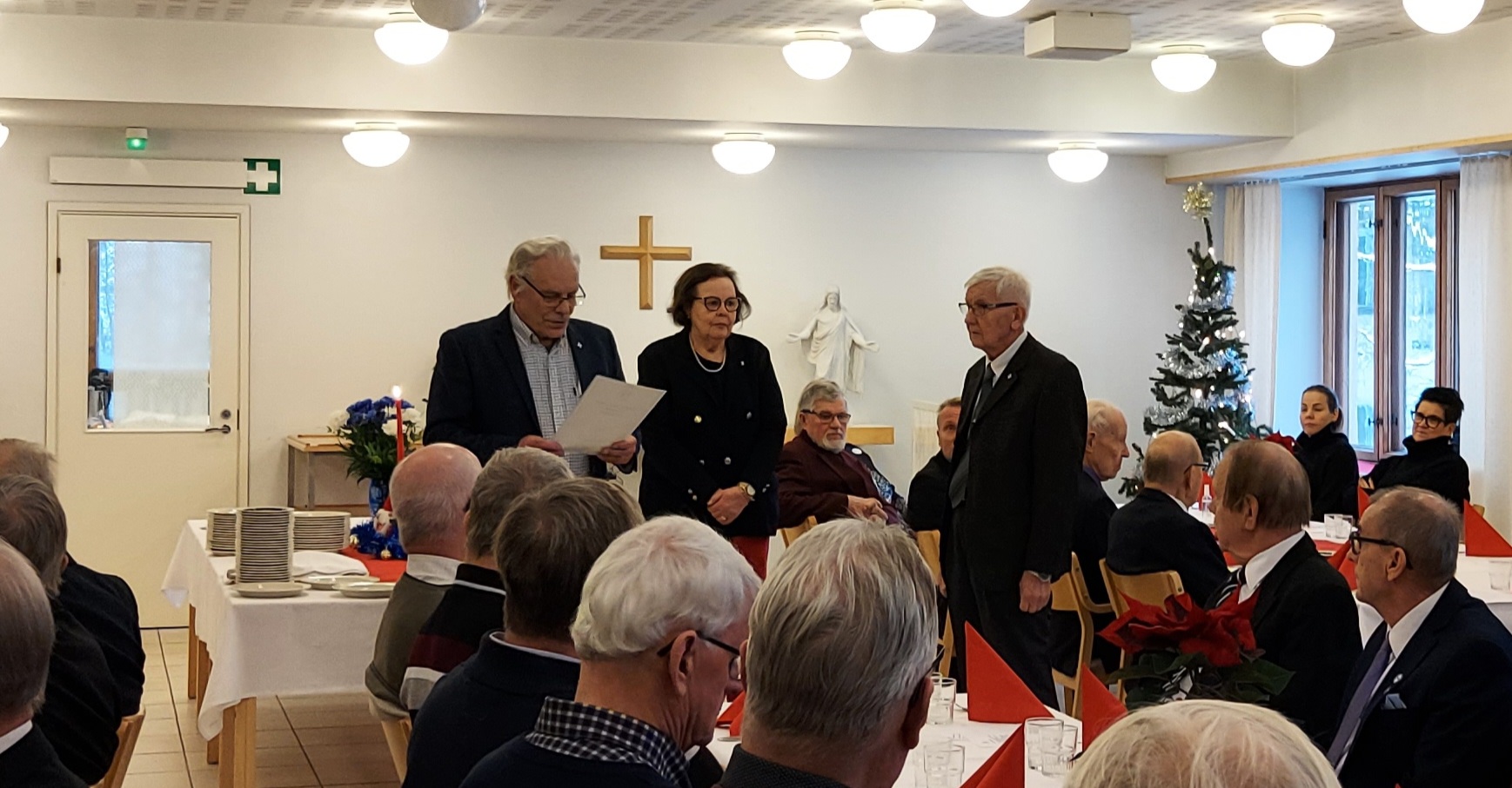 Kolme ihmistä juhlavieraiden edessä.