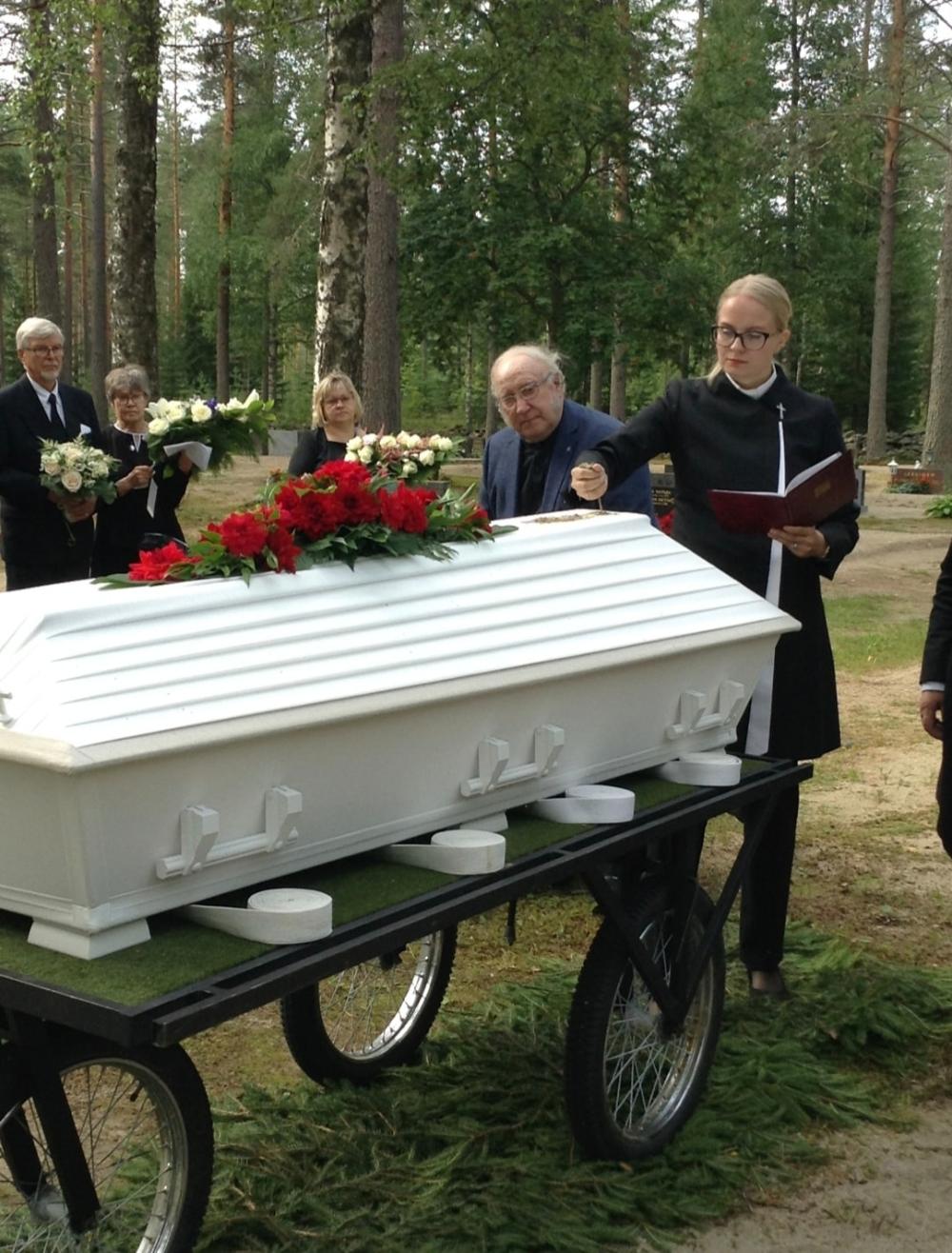 Hautajaiset hautausmaalla, lähikuvassa arkku ja pappi.