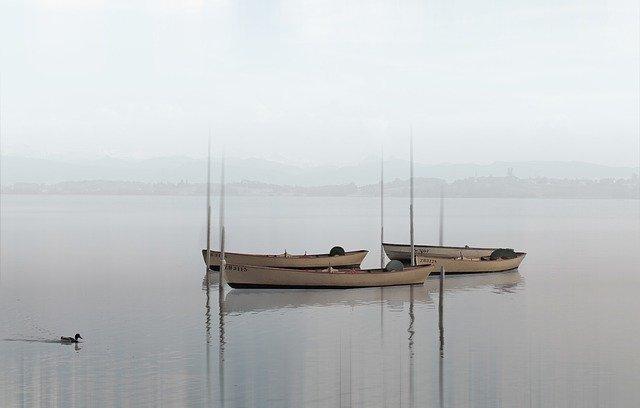 kolme tyhjää venettä sumuisella järvellä.