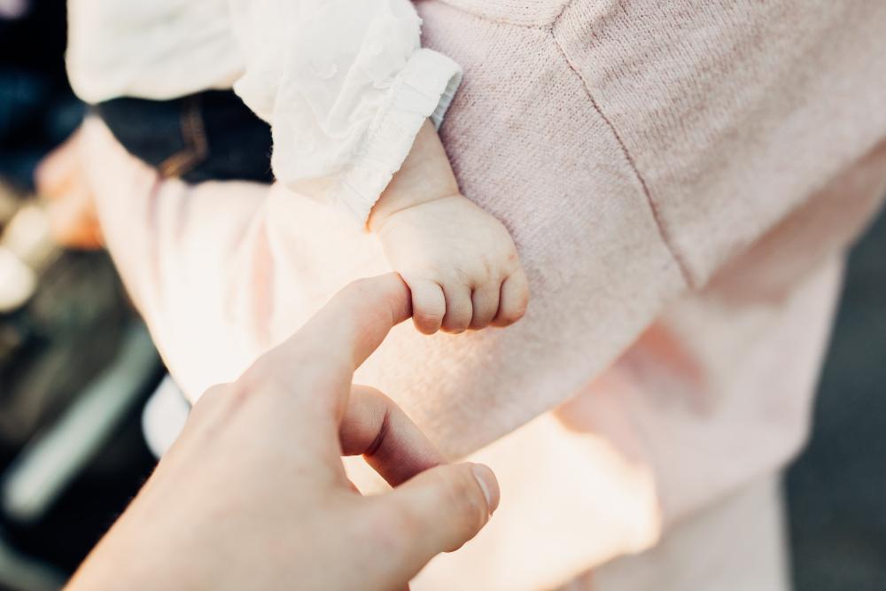 Aikuisen käsi pitää kiinni vauvan kädestä.