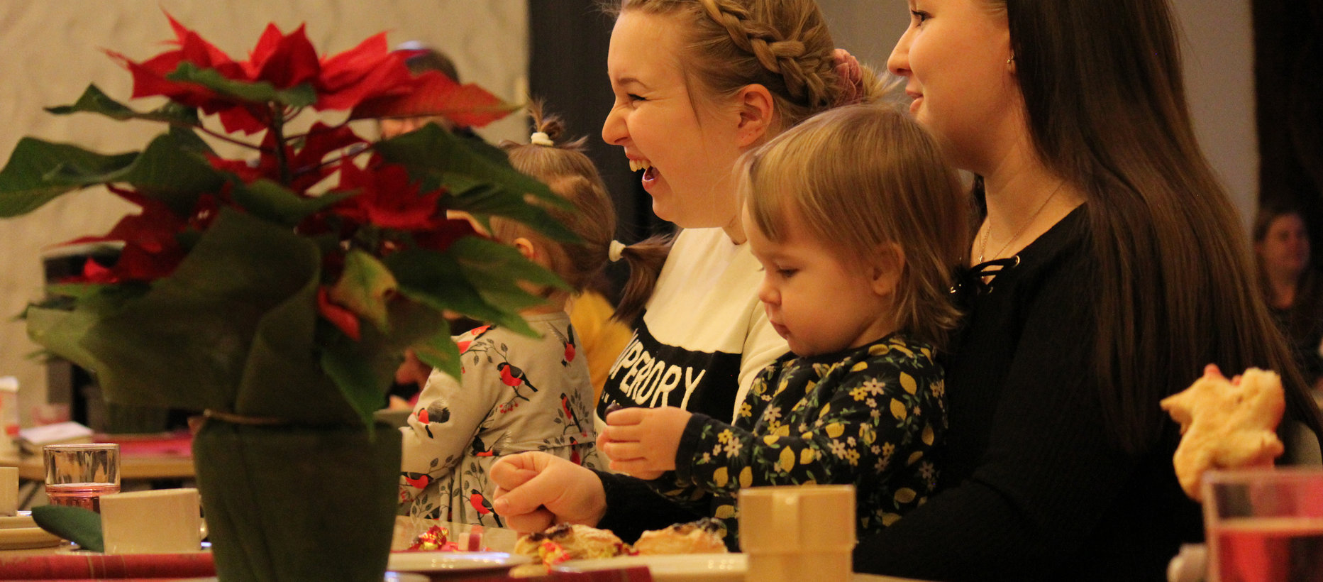 Iloiset äidit lapset sylissä istumassa Kuoppakankaan seurakuntasalin kahvion pöydässä.