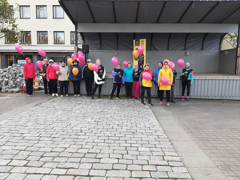 Naisia värikkäissä ulkoiluvaatteissa ja pinkit ilmapallot käsissään.