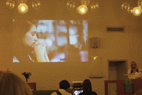 Esirukouksen aikaan seinälle heijastettiin kuva rukoilevasta nuoresta naisesta.