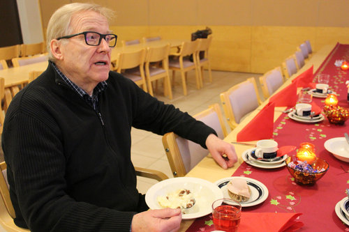 Juhani istuu punaisin liinoin ja kynttilöin katetussa kahvipöydässä.