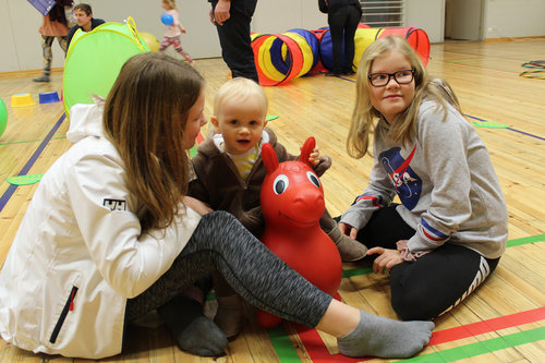 Sisarusten nuorimmainen punaisen pommpulelun päällä istumassa.