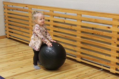 Tyttö vierittää pientä jumppapalloa liikuntasalissa.