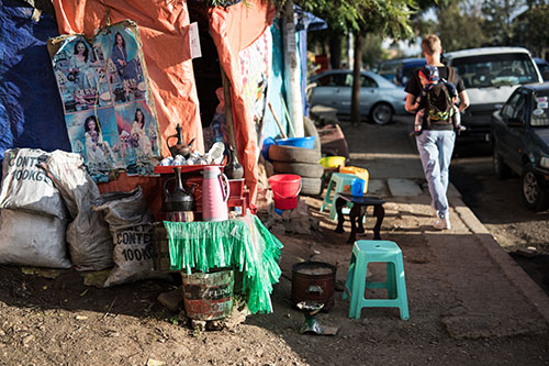 Mien kävelee lapsi selässä rinkassa afrikkalaisen pääkaupungin kadun varressa olevan myyntikojun ohitse.