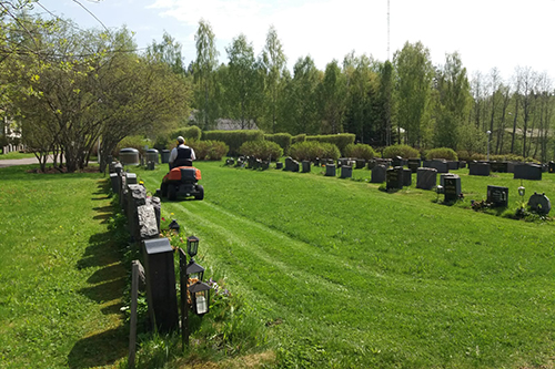 Kesätyöntekijä ajaa päältäajettavalla ruohonleikkurilla ruohoa.