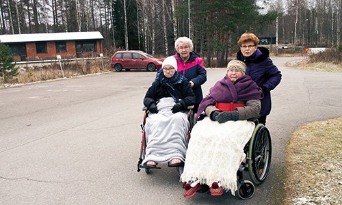 Naiset työntämässä kahta iäkkäämpää naista pyörätuoleilla.