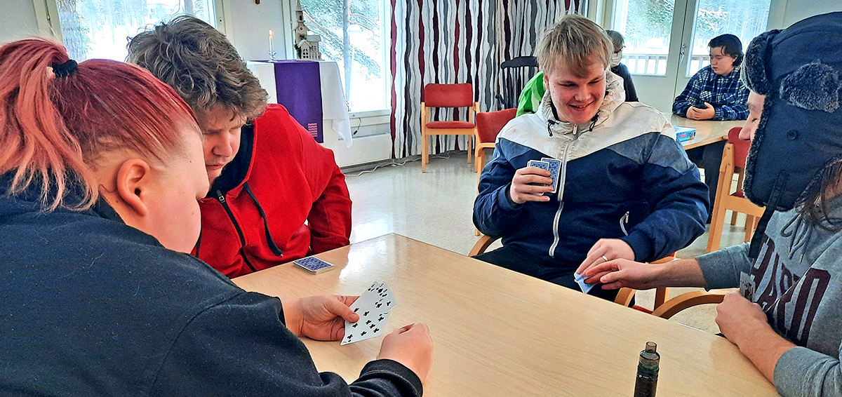 Korttia pelaavat nuoret, taustalla käydään kahdenkeskistä keskustelua.